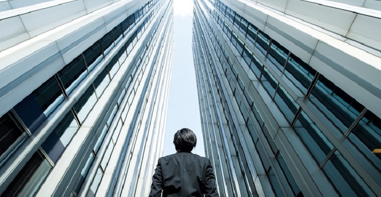 Businessman surrounded by tall steel buildings looks to the sky