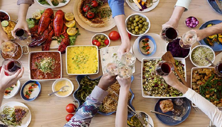 A table loaded with food from many different cultures, and hands reaching in towards the food.