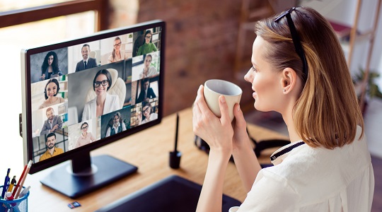 Woman seated at a desk drinking a coffee, while participating in a video conference