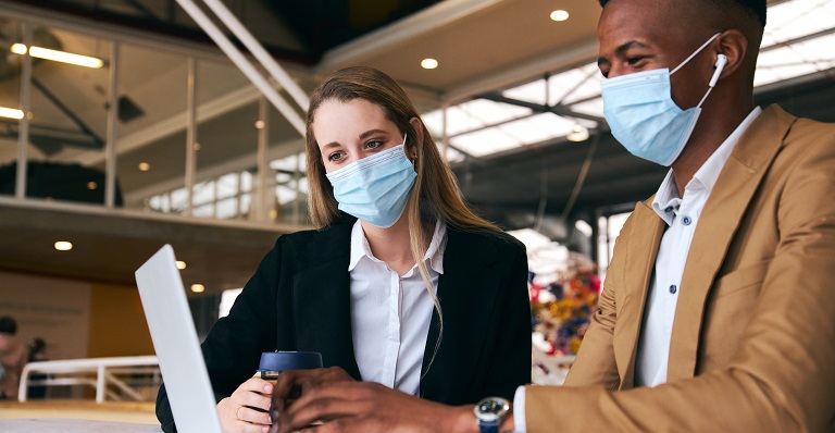 Business couple wearing masks work on laptop