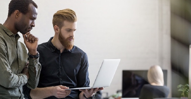 Two worried businessmen look at laptop while standing in an office