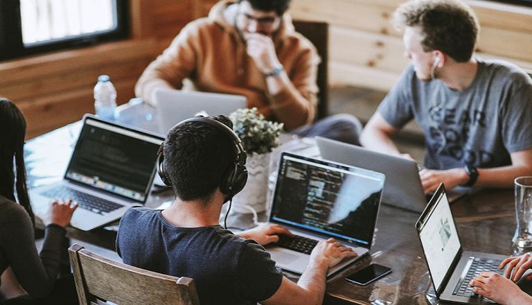 Five people work on laptops and exchange ideas in a shared workspace.