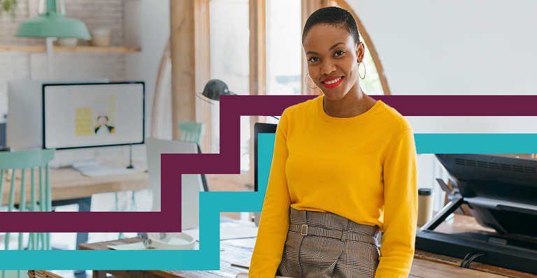 Diverse woman sitting on desk looking directly at camera.