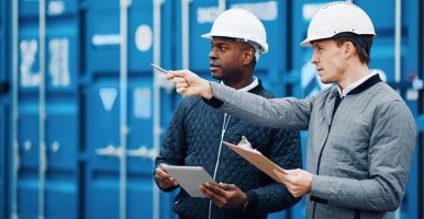 Two men in hard hats stand in front of blue shipping containers