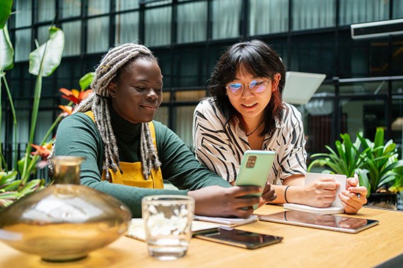 Image de deux femmes, avec téléphone cellulaire, cahier de notes et tablettes, épanouies dans un milieu de travail inclusif et équitable.