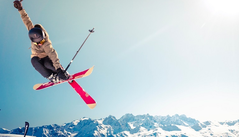 A skier takes an impressive leap on a bright, snowy hilltop.