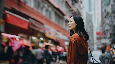 Une dame au regard pensif, debout sur une rue passante entourée de gratte-ciel