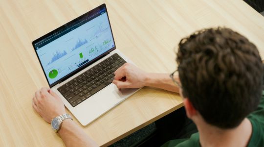 Man viewing charts and diagrams on a laptop from the back.
