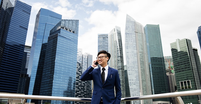 Un homme asiatique souriant se tient devant les gratte-ciel de Bangkok
