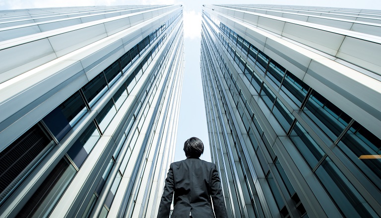 Businessman surrounded by tall steel buildings looks to the sky