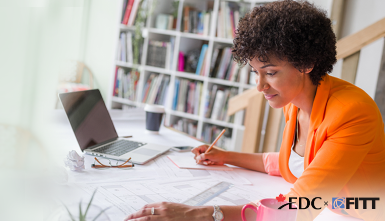 Woman writing on a notepad while working at her desk with a laptop.