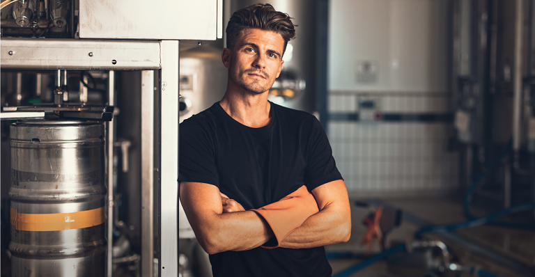 A microbrewery owner stands next to industrial equipment.